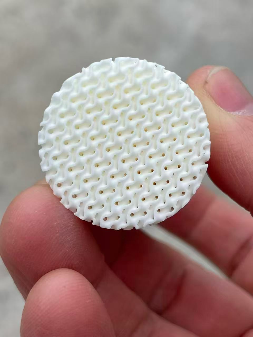 Close-up of a custom porous YSZ zirconia ceramic disc with an interconnected open-cell structure.