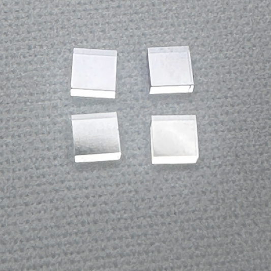 Four square-shaped, silver-colored diamond single crystal wafers/substrates arranged on a textured grey surface.